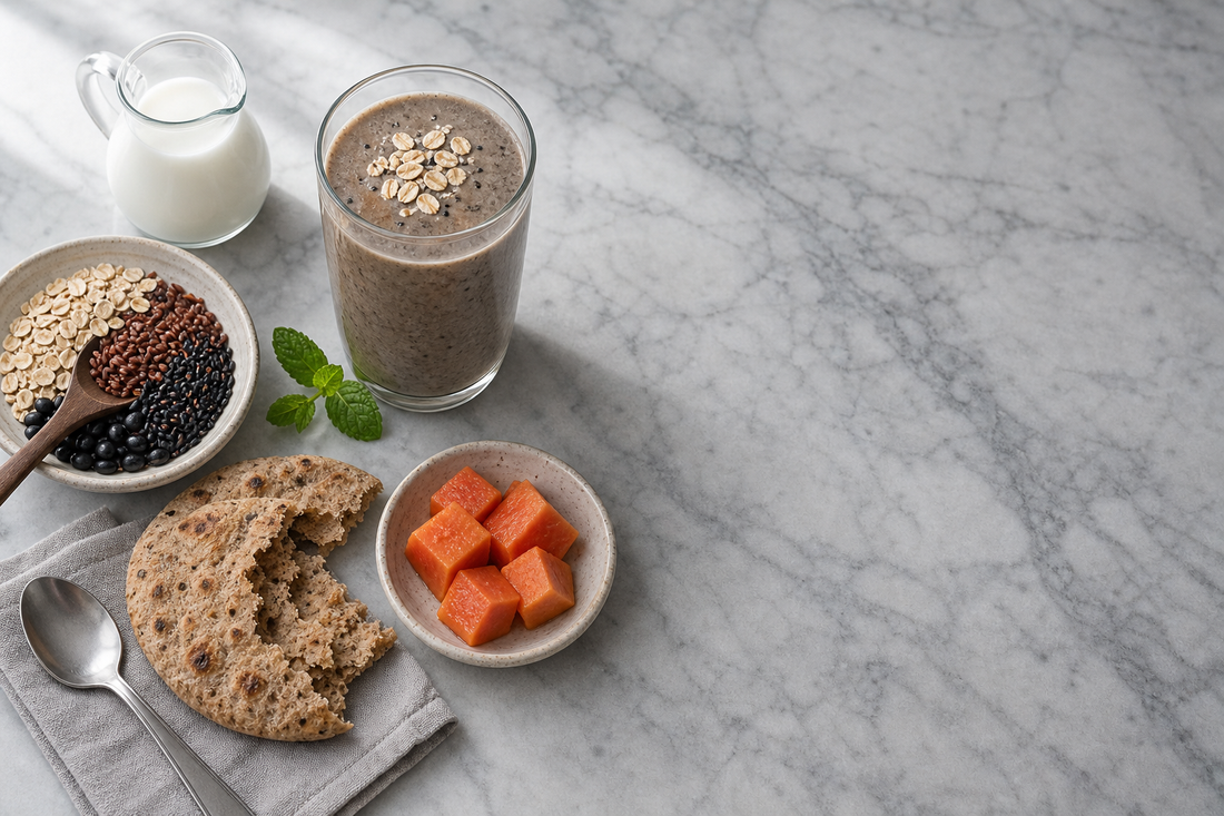 Editorial flat-lay on cool-grey marble of a wholesome oat and black sesame meal replacement drink with a bowl of mixed whole grains, wholemeal roti, papaya and mint — for a Malaysian meal replacement guide.